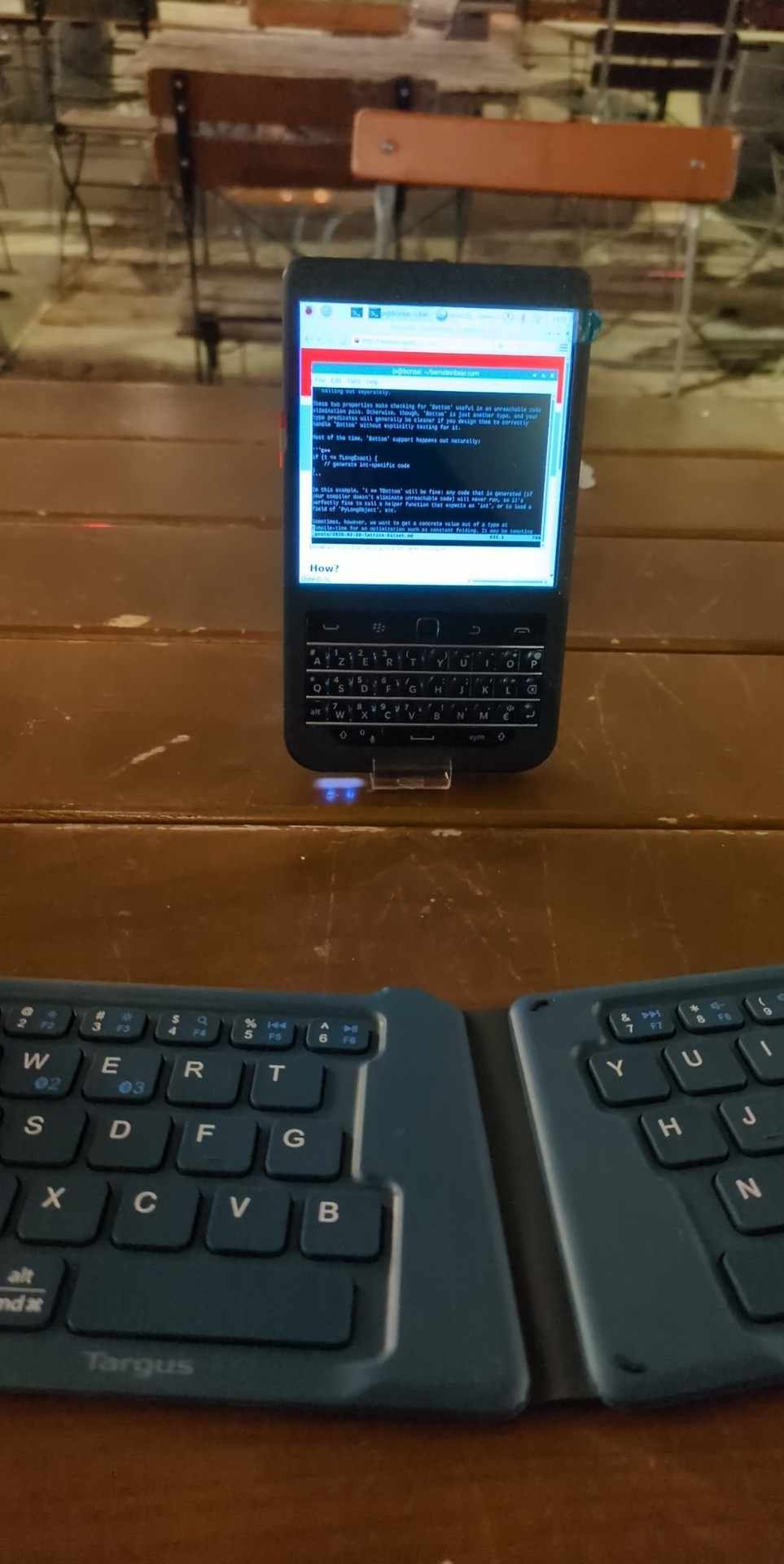 Hackberry Pi (blackberry keyboard with small lcd powered by raspberry pi) standing up in the background with a split wireless keyboard in the foreground. I'm an an outside table of a cafe at night.